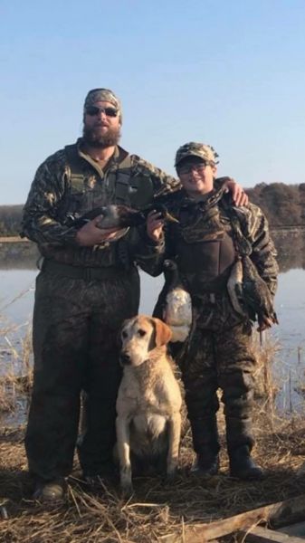 2 people in camouflage posing with their dog