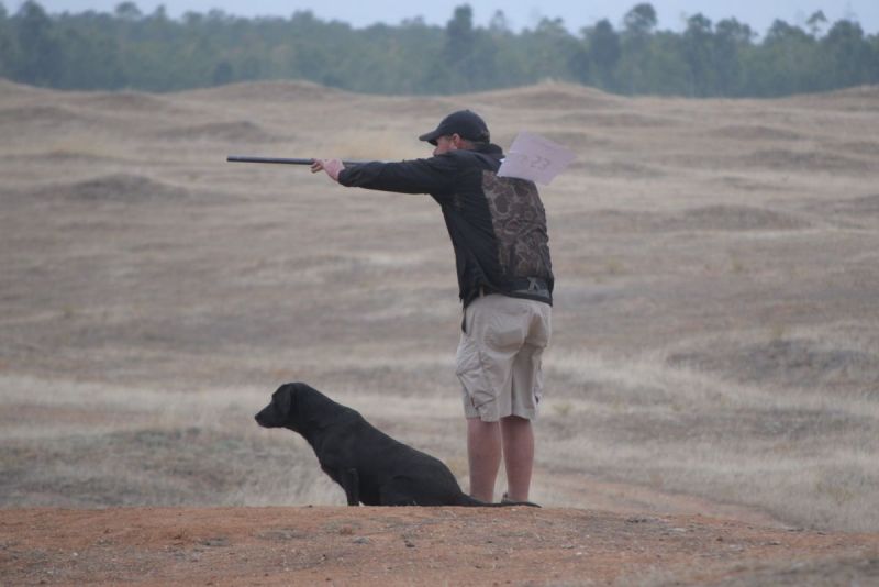 man shooting with dog next to him