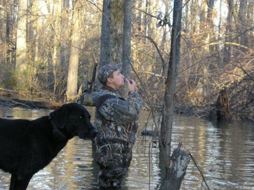 man with duck call and dog in swamp
